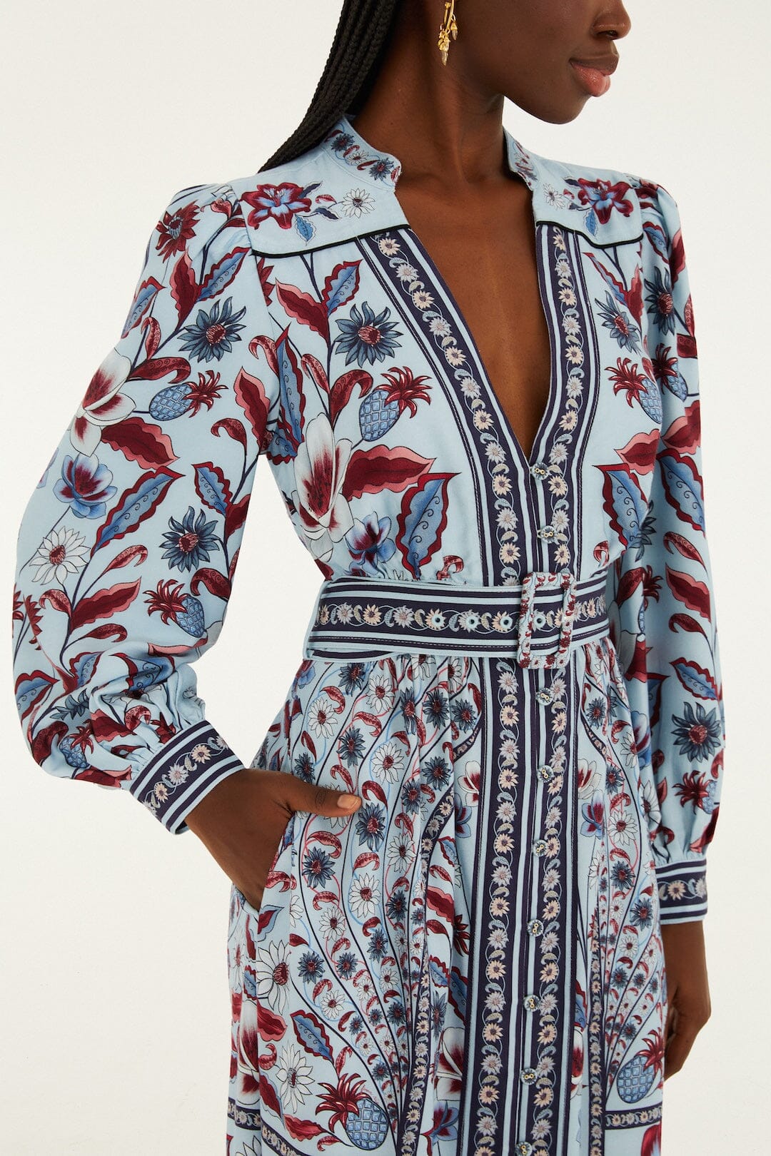 Wearing the Farm Rio Marcelle Maxi Dress—a long-sleeve soft blue dress with a deep V-neck, red, blue, and white floral patterns, a fitted waist, and handy pockets.