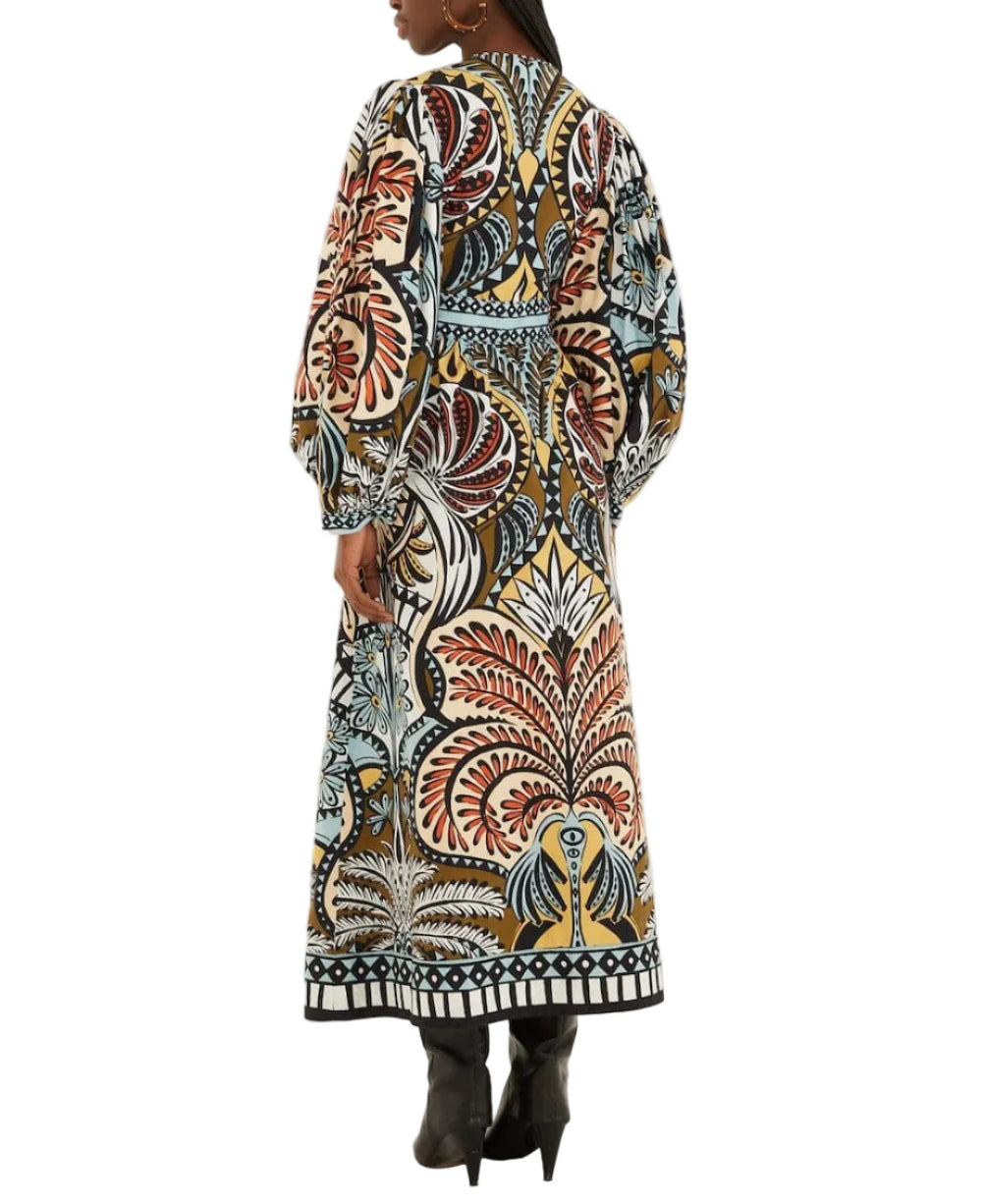 A woman in the Farm Rio Balamana Maxi Dress—long, loose-fitting, with a vibrant multicolored botanical print and long sleeves—pairs it with black boots and faces away from the camera. Perfect for your next tropical getaway.