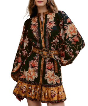 Woman wearing the Majestic Garden Black Mini Dress by Farm Rio—a floral print mini dress featuring long sleeves, a beaded buckle belt, and ruffled hem in bold black, gold, and orange.