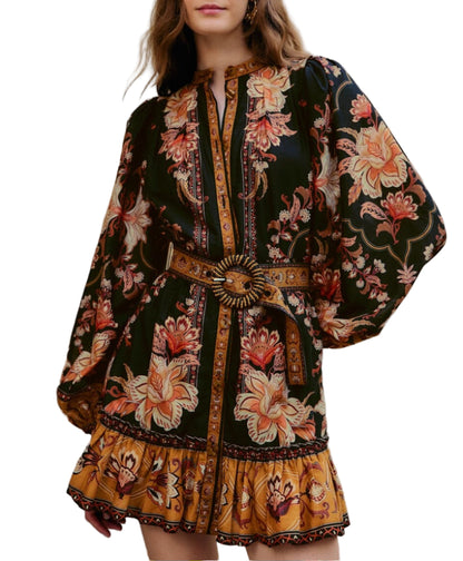 Woman wearing the Majestic Garden Black Mini Dress by Farm Rio—a floral print mini dress featuring long sleeves, a beaded buckle belt, and ruffled hem in bold black, gold, and orange.