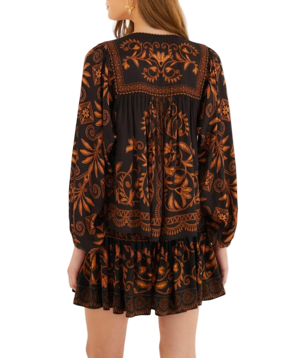 A woman is shown from the back wearing the Farm Rio Cornely Ainika Blouse—a black top with black and gold florals, long sleeves, and a ruffled hem.
