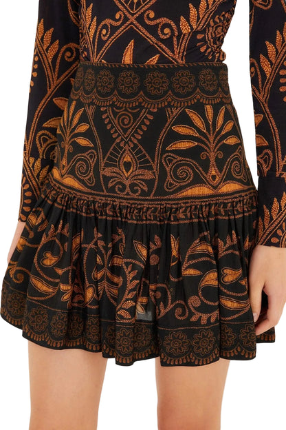 A person wears the Farm Rio Cornely Ainika Skirt and matching long-sleeve top, both in black with orange and gold floral patterns—an ideal resort-ready outfit.