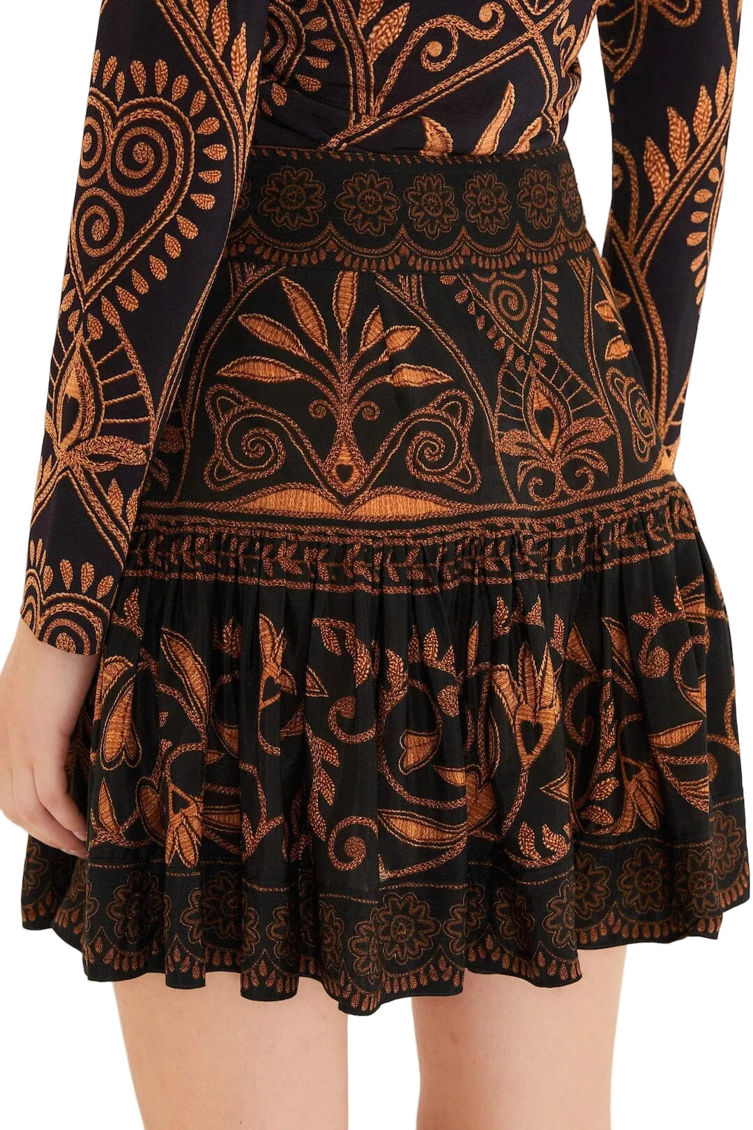 A person wears the Farm Rio Cornely Ainika Skirt, a black skirt with detailed orange and gold floral and geometric patterns, shown from the back waist down.