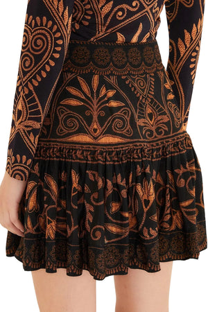 A person wears the Farm Rio Cornely Ainika Skirt, a black skirt with detailed orange and gold floral and geometric patterns, shown from the back waist down.