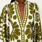 A woman wears the Farm Rio Palermo Green Maxi Dress, featuring a buttoned puff sleeve design, olive floral patterns, and a deep V-neckline with white front buttons.