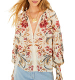 Woman wearing a long-sleeve Royal Garden Sand Blouse by Farm Rio with a V-neck and light blue jeans, accessorized with a gold necklace. This blouse brings elegant style to her casual look.