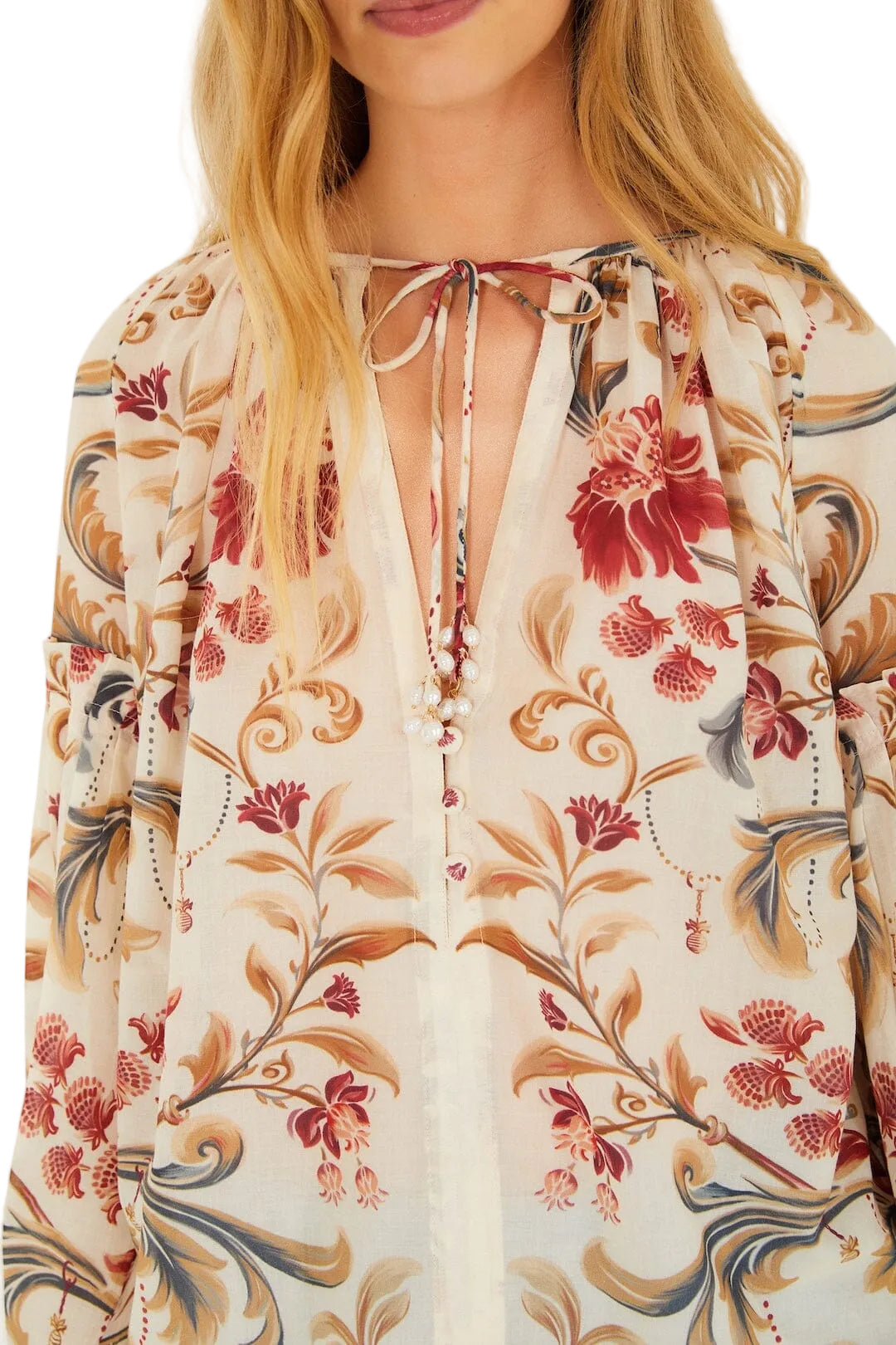 A woman wears the Farm Rio Royal Garden Sand Blouse, showcasing a floral print, tie neckline, and pearl details, pictured from shoulders to mid-torso.