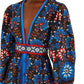 A woman wears the Farm Rio Latina Scarf Mini Dress, featuring long sleeves, a deep V-neck, and a blue, red, and white floral pattern on a dark background.