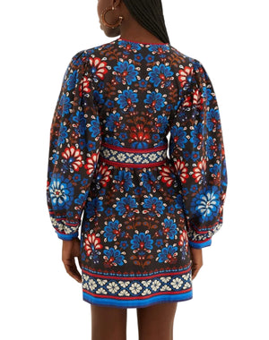A woman faces away, wearing the Farm Rio Latina Scarf Mini Dress—this chic mini features long puffed sleeves and a vibrant blue, red, and white floral print, perfect for a stylish beach party look.