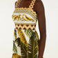 A woman wears the Farm Rio Trancoso Sand Sleeveless Maxi Dress, an eco-friendly piece featuring a scalloped neckline and a banana leaf and fruit print in green, yellow, and beige tones.