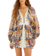 Woman wearing the Farm Rio Sea Garden Off White Mini Bubble Dress, featuring long sleeves, a flowy silhouette, deep V-neck, and subtle puff sleeves for a chic bohemian look.