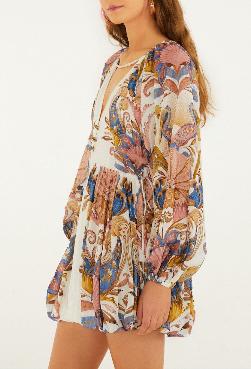 Woman wearing the Sea Garden Off White Mini Bubble Dress by Farm Rio, featuring puff sleeves, a floral and leaf print, deep V-neckline, elastic waist, and blue, pink, and gold tones.