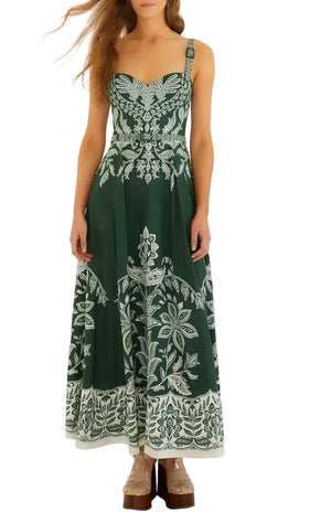 A woman wears the Farm Rio Miranda Dark Green Belt Buckles Maxi Dress, featuring a sleeveless design with white floral patterns, styled with platform shoes against a white background.