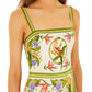 A woman wears the Farm Rio Sand Tropical Scarf Sleeveless Mini Dress, a premium linen mini with green trim and a vibrant botanical and parrot print.