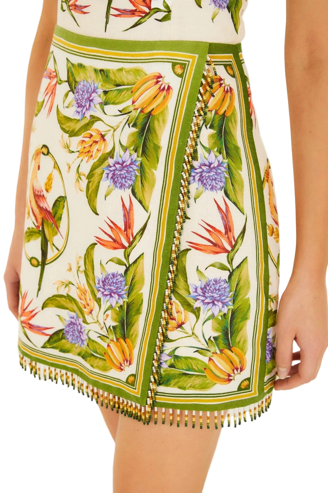 A close-up of the Farm Rio Sand Tropical Scarf Sleeveless Mini Dress, showcasing its vibrant floral print, green borders, and bead fringe detailing along the hem.