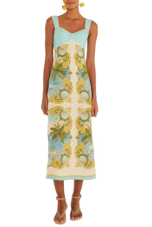 A woman wears the Farm Rio Royal Sea Multicolor Maxi Dress, a sleeveless Euroflax linen style with a turquoise bodice and tropical patterned skirt in yellow, green, and blue, paired with sandals and earrings.