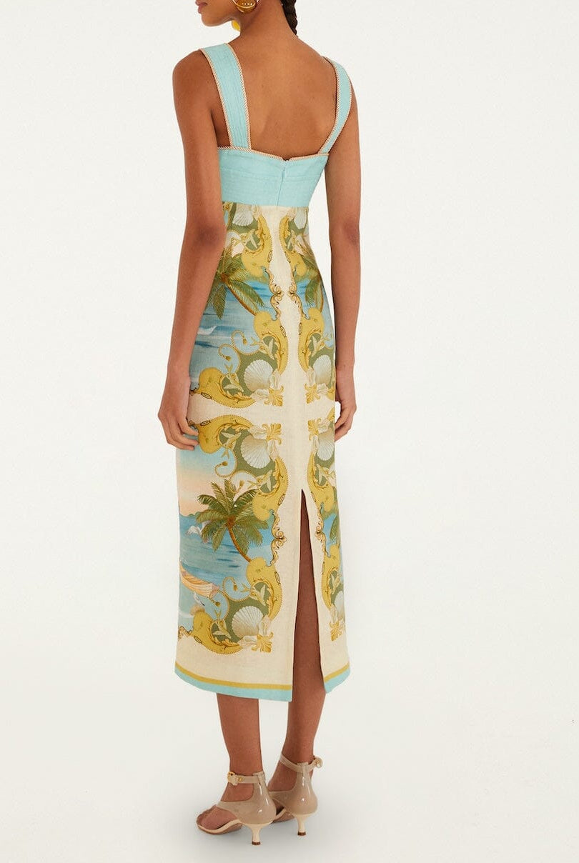 A woman stands facing away in the Farm Rio Royal Sea Multicolor Maxi Dress—a sleeveless, fitted linen dress with a blue bodice, ornate multicolored skirt, and sweetheart neckline—paired with heeled sandals.