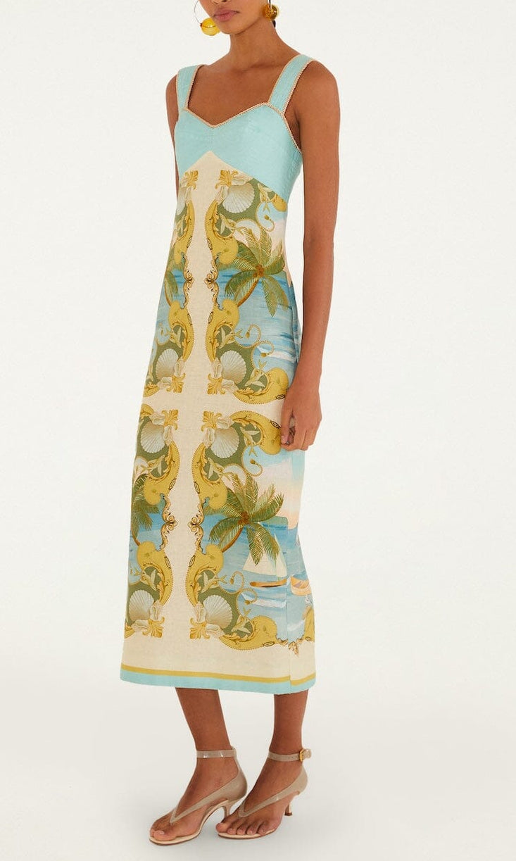 A woman wears the Farm Rio Royal Sea Multicolor Maxi Dress, featuring a sleeveless design with a blue and yellow baroque and palm leaf pattern, sweetheart neckline, paired with beige sandals.