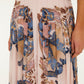A person wears the Farm Rio Sea Garden Scarf Soft Pink Maxi Skirt, featuring a blue, pink, and brown floral and abstract print; their right hand rests by their side.