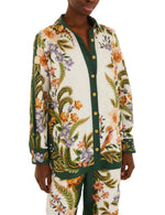 A person wearing the Farm Rio Nature Sand Shirt with matching pants, featuring a colorful floral and bird print on a white and green background.