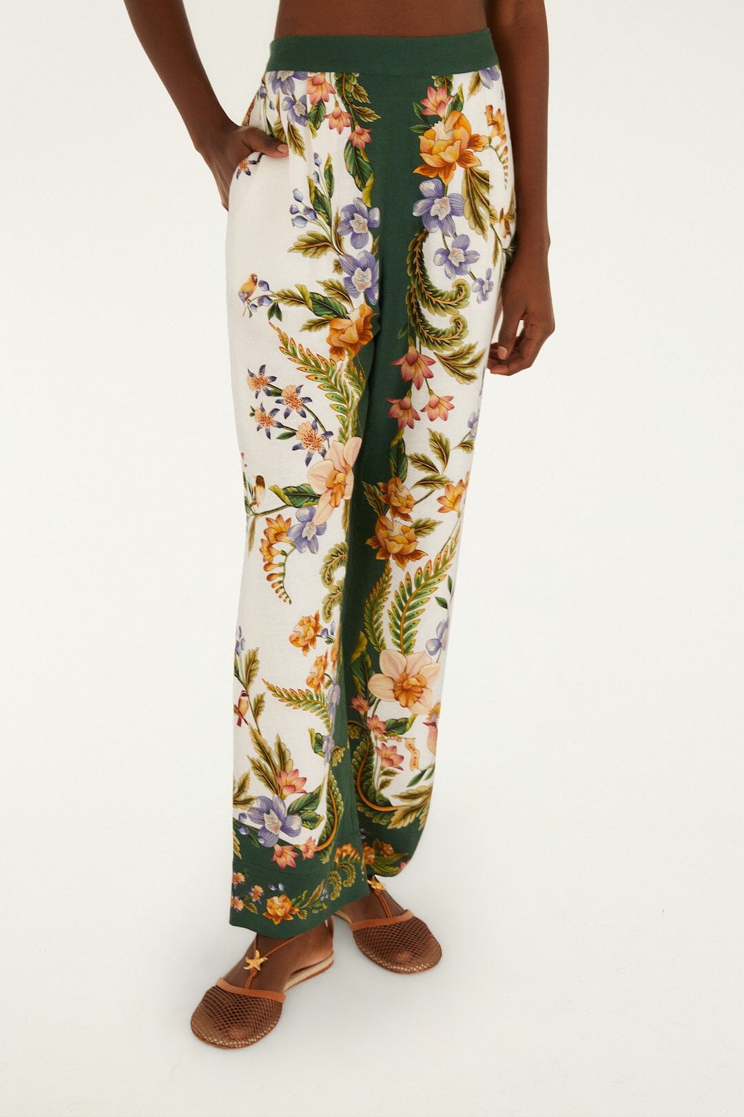 Someone wears Farm Rio Nature Sand Pants—high-waisted, wide-leg with a green and white floral print—paired with brown woven flat shoes.