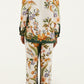A person stands facing away, wearing a matching long-sleeve top and Farm Rio Nature Sand Pants, which feature a colorful floral pattern on a white background.