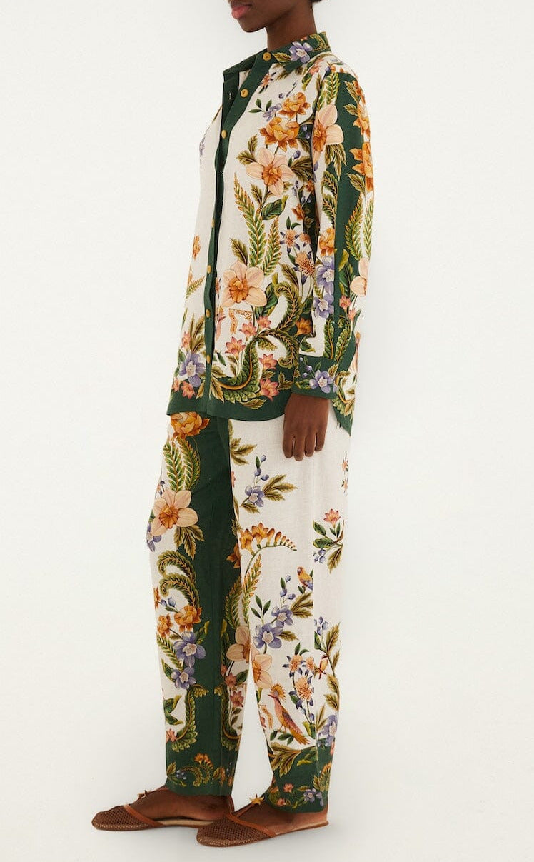 A person stands sideways against a plain white background, wearing Farm Rio’s Nature Sand Pants as part of a matching floral print pajama set with wide-leg pants and long sleeves.