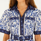Woman wearing the Porcelain Garden Off White Mini Dress by Farm Rio, featuring blue and white florals, short sleeves, front buttons, chest pockets, and a belted waist.
