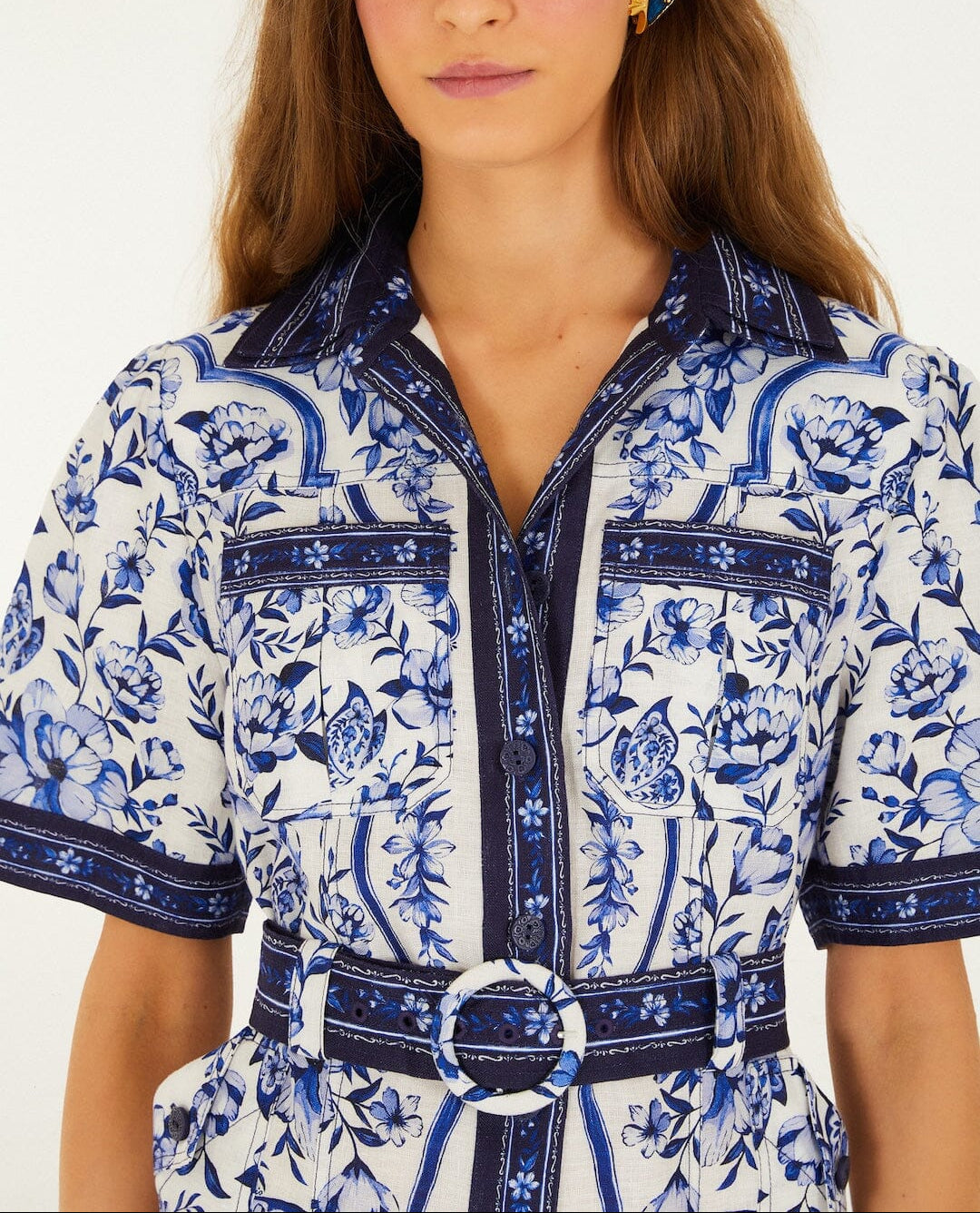 Woman wearing the Porcelain Garden Off White Mini Dress by Farm Rio, featuring blue and white florals, short sleeves, front buttons, chest pockets, and a belted waist.