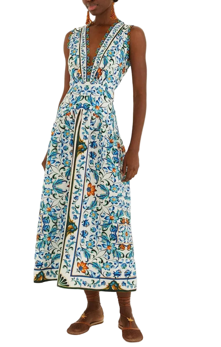 A person wears the Farm Rio Flora Tile Off White Midi Dress, which features a blue, green, and orange floral tile pattern, paired with brown flat shoes.