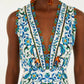 A person wearing the Farm Rio Flora Tile Off White Midi Dress, featuring a sleeveless V-neck, blue and green floral tile print, scalloped hem, and orange drop earrings.