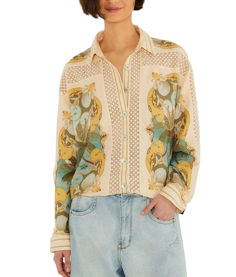 A woman wears the Farm Rio Royal Sea Crochet Detail Shirt, a light-colored button-up with a floral and bird print in an Ecovero blend, paired with light blue jeans and standing with one hand in her pocket.