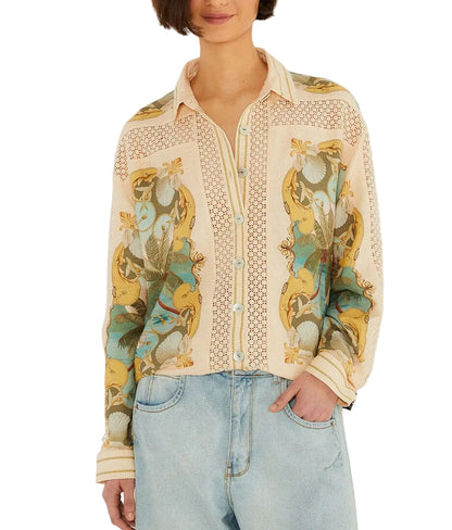 A woman wears the Farm Rio Royal Sea Crochet Detail Shirt, a light-colored button-up with a floral and bird print in an Ecovero blend, paired with light blue jeans and standing with one hand in her pocket.