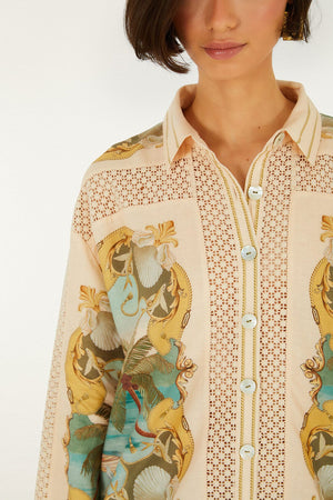 A woman wears the Royal Sea Crochet Detail Shirt by Farm Rio—a patterned button-up with gold, blue, and beige designs in an Ecovero blend. Featuring a collar and visible buttons, it's ideal for lightweight layering. Her face is partially out of frame.