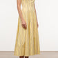 A woman wears the Staud Wells Monday Stripe Lobster Dress—a sleeveless, yellow cotton poplin dress with vertical black stripes—and black sandals, standing on a smooth light brown floor against a plain white background.