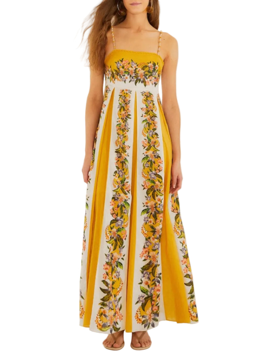 A woman wears the Farm Rio Sand Hilo Stripes Dress, a sleeveless, floor-length yellow and white dress featuring floral vertical stripes and thin shoulder straps.
