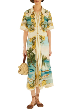 A woman wears the Farm Rio Royal Sea Multicolor Midi Dress with nature-inspired patterns and a tie belt, paired with a beige textured handbag and brown flat sandals.