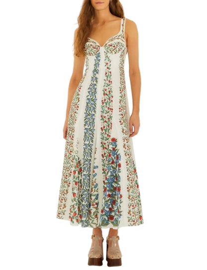 A woman wears the Fruit Beauty Off White Dress by Farm Rio, a sleeveless, ankle-length style with colorful floral patterns, paired with beige platform sandals.