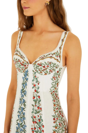 A woman wears the Fruit Beauty Off White Dress by Farm Rio—a sustainable sleeveless maxi dress with colorful floral embroidery featuring green leaves and red, orange, and blue flowers.