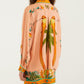 A person wearing a Farm Rio Birds Canto Dos Passardos Shirt, peach-colored with two long-tailed birds and green leaves printed on the back, paired with a matching floral skirt.