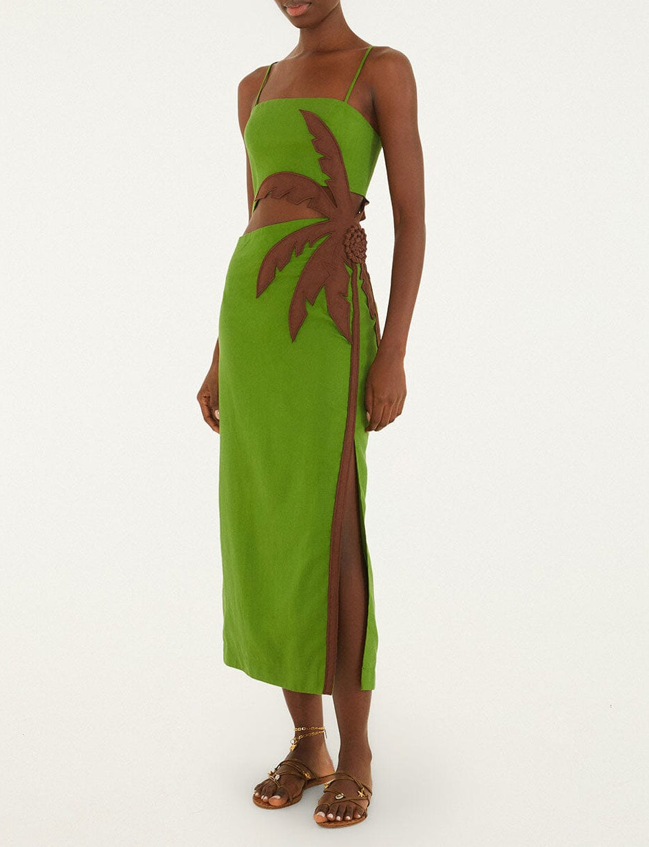 A person wears the Farm Rio Green Palm Tree Maxi Dress, featuring a brown leaf appliqué and side cutout, paired with flat sandals, standing against a plain background.