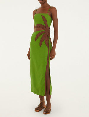 A person wears the Farm Rio Green Palm Tree Maxi Dress, featuring a brown leaf appliqué and side cutout, paired with flat sandals, standing against a plain background.