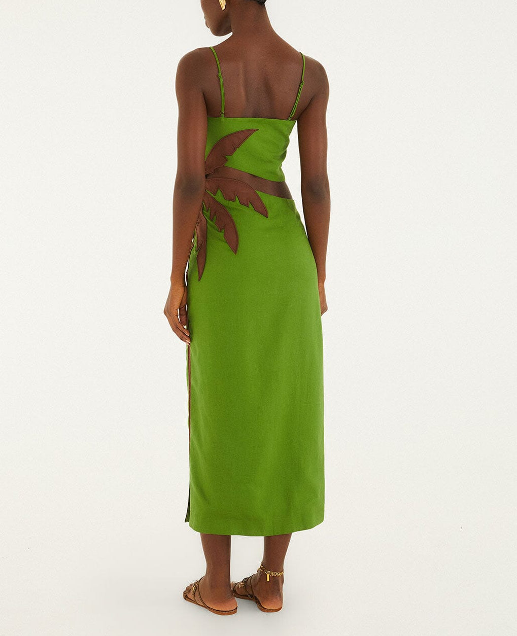 A person in a Farm Rio Green Palm Tree Maxi Dress with brown side leaf detail and flat sandals stands against a white background, facing away from the camera for a fresh, modern tropical look.