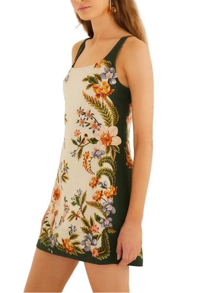 A woman wears the Farm Rio Nature Sand Mini Dress, a sleeveless mini with a white center panel, green sides, and a vibrant floral pattern.