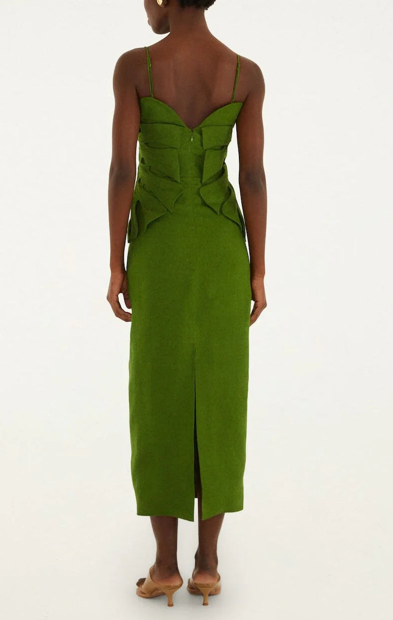 A person models the Green Monstera Leaf Maxi Dress by Farm Rio—fitted, sleeveless, with sculptural details and a sweetheart back neckline—standing on a white background, facing away from the camera.