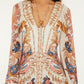 A woman wearing the Farm Rio Sea Garden Off White Braid Details Long Dress, featuring floral and paisley designs in pink, blue, and gold, accessorized with a necklace and drop earrings.