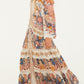 A woman wearing the Farm Rio Sea Garden Off White Braid Details Long Dress walks to the left, paired with flat woven shoes.