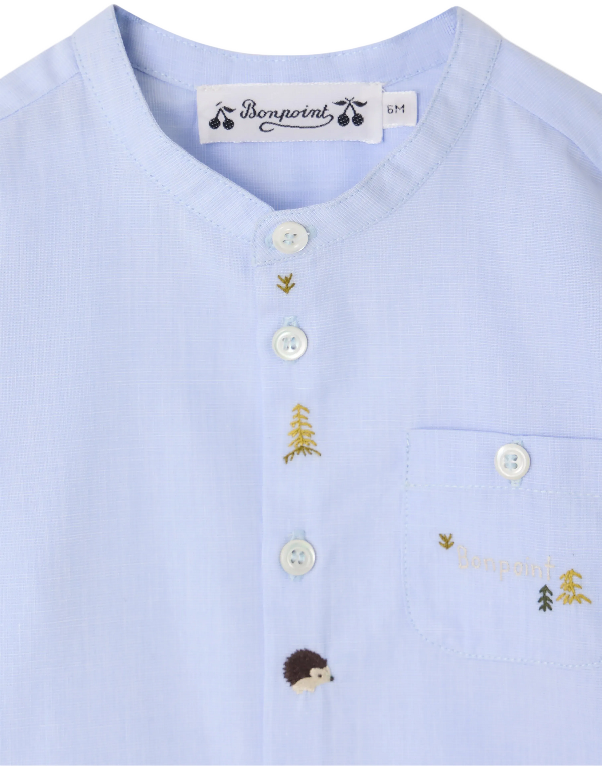 The Baby Boys’ and Boys’ Matis Shirt by Bonpoint is a light blue shirt for babies, detailed with white buttons, a small hand-embroidered hedgehog and fir trees, and “Bonpoint” text above the pocket.