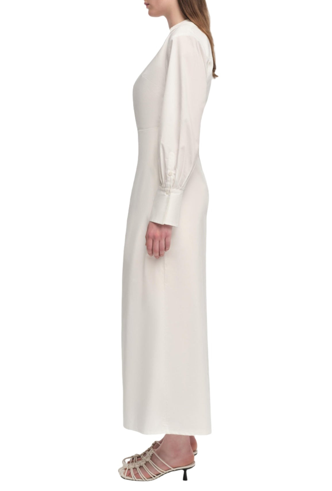 Person wearing a long white Simkhai Briar Dress with long sleeves and white heeled sandals, viewed from the side.