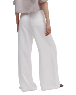 With their back to the camera, the person wears TWP Dee's Trouser—relaxed high-rise wide leg pants in a light shade—paired with a soft-toned top.